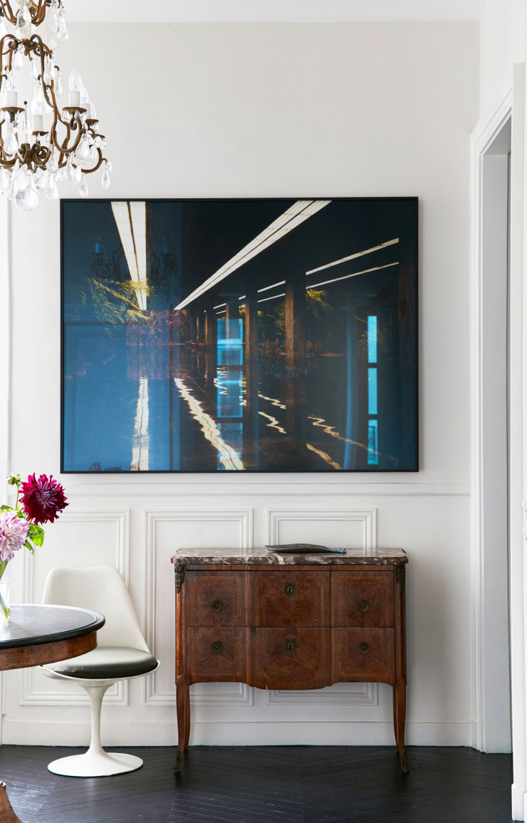 Dans le corridor, le parquet a été repeint en bleu marine profond. Console du XIXe. Photo de l’artiste américaine Taryn Simon. Le lustre en cristal de roche et la table avec plateau en marbre datent du XIXe. Tulip Chair (Knoll, 1956) d’Eero Saarinen.