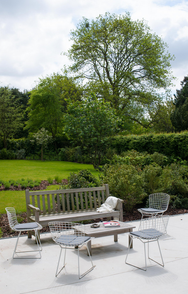 Sur la terrasse, banc et table basse (Tectona), chaises Wire de Harry Bertoia (Knoll). Le jardin a...