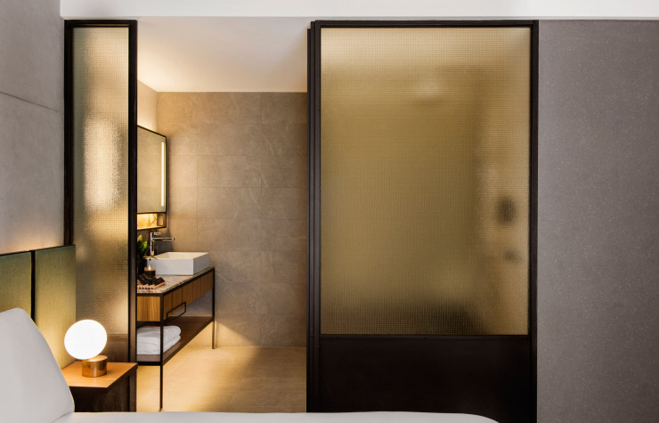 Une paroi en verre doré sépare la chambre à coucher de la salle de bains.