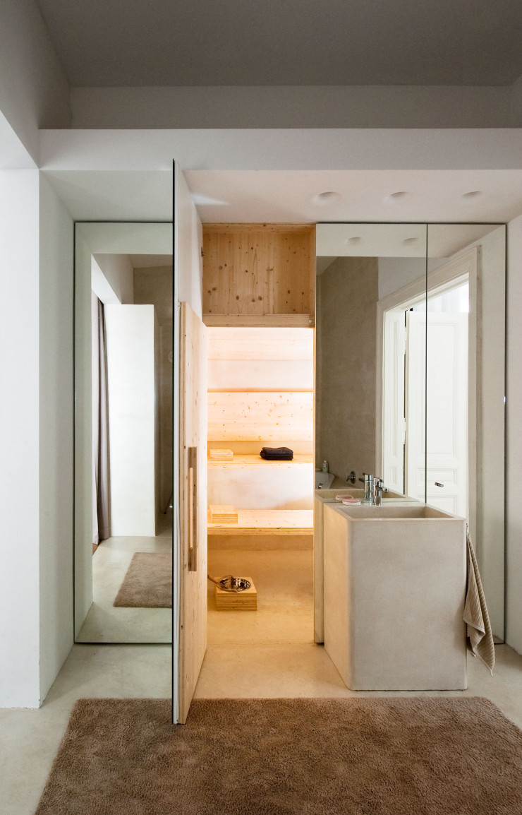 Dans la salle de bains aux murs habillés de miroirs, le sol et le lavabo (sur mesure) sont recouverts de dalles de ciment dont l’aspect évoque le béton ciré (Pandomo). Tapis Poodle (Object Carpet). Sauna Birchwood.